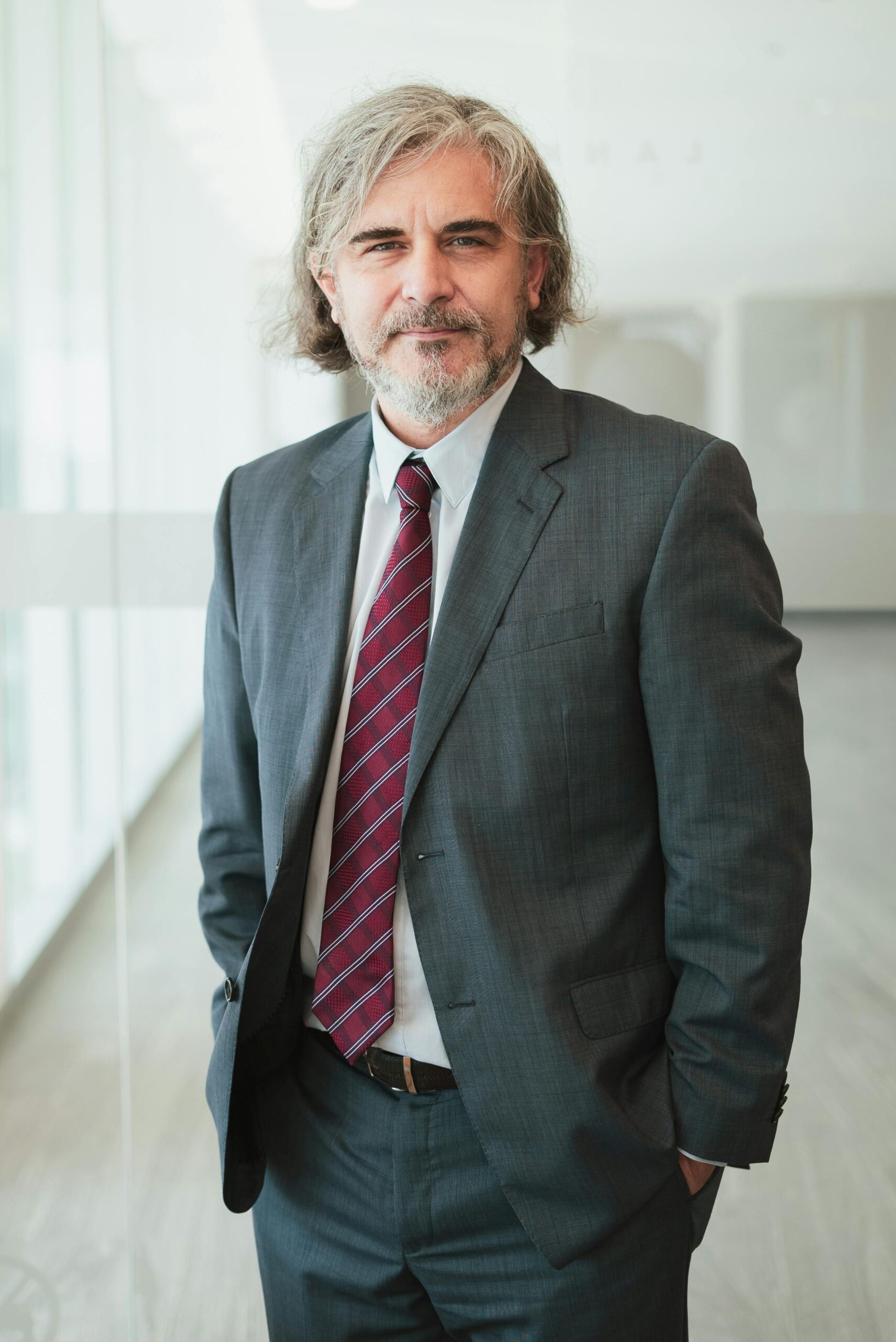 pexels-photo-10041269-10041269 Mature man with gray hair and beard in corporate office setting, wearing a suit and tie.